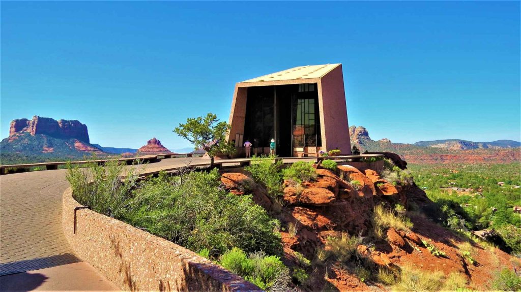 Scenic vista in Sedona, Arizona, ideal for couples, featuring towering red rock formations against a clear blue sky. A winding trail leads through desert flora and cacti, offering secluded spots with panoramic views. The warm hues of the landscape create a romantic setting, perfect for couples to explore and enjoy the natural beauty together.