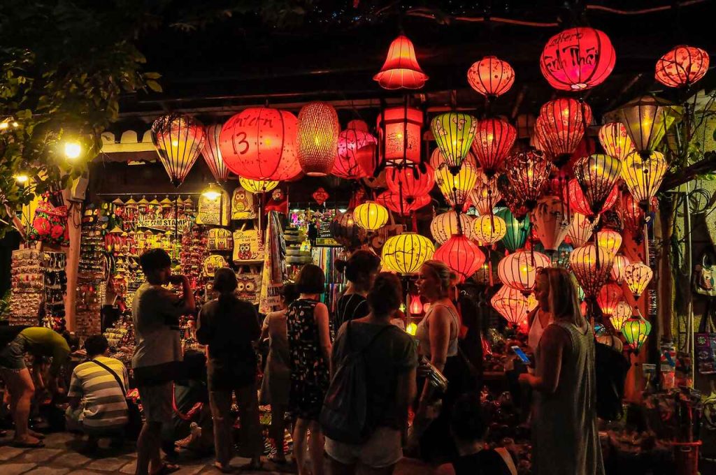 An aerial view of Hoi An’s ancient town, a UNESCO World Heritage site, showcasing its preserved traditional architecture with yellow-walled buildings, wooden houses, and lantern-lit streets along the Thu Bon River, capturing the town's timeless charm and cultural heritage.